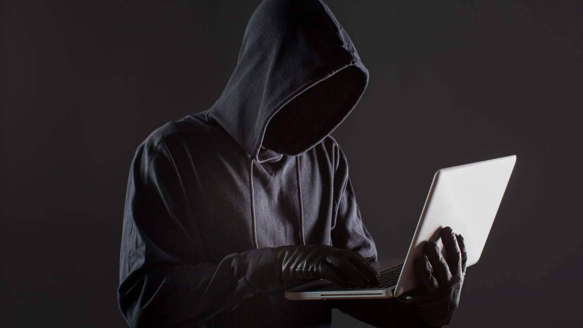hacker wearing hoodie holding laptop while wearing gloves