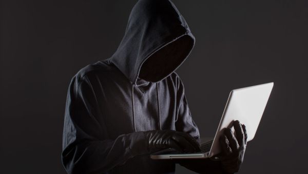 hacker wearing hoodie holding laptop while wearing gloves